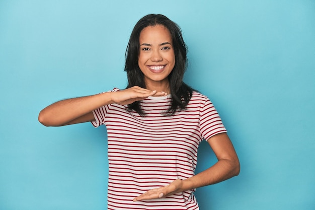 Filipina young woman on blue studio holding something with both hands product presentation