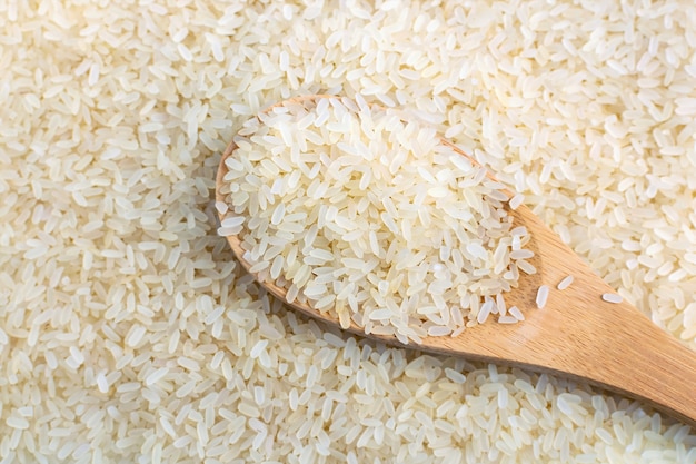 Filled wooden spoon with uncooked parboiled white rice close-up. Long grains, organic natural healthy food top view.