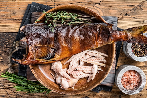 Fillet of Hot smoked fish pike perch or zander in a wooden plate with herbs. wooden background. Top view.