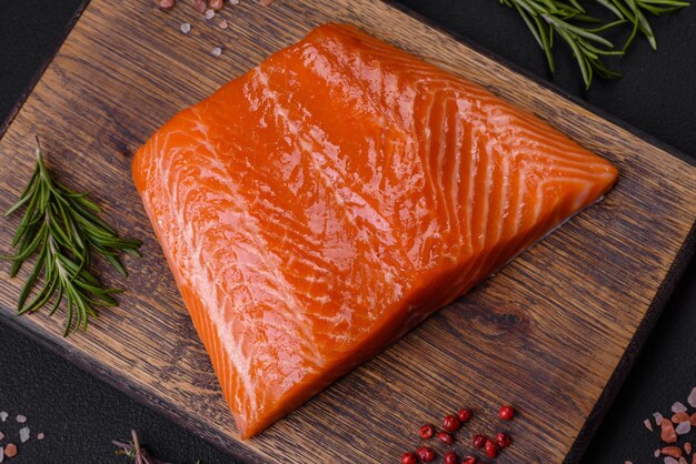 Fillet of raw red salmon fish with salt spices and herbs on a dark concrete background