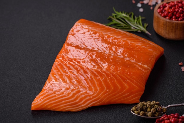 Fillet of raw red salmon fish with salt spices and herbs on a dark concrete background