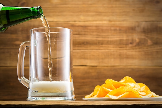 Filling a glass with beer on wooden wall.