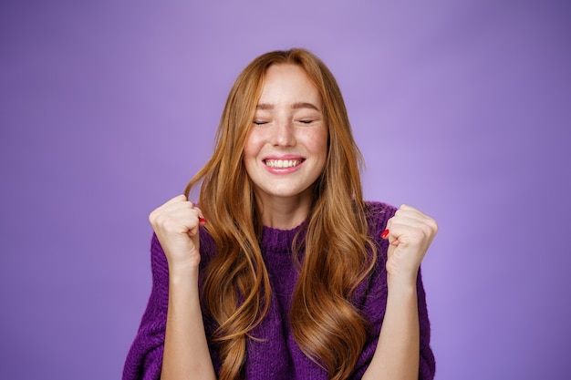 Finally I won. Portrait of relieved and happy triumphing good-looking redhead woman clenching fists in joy and happiness, celebrating victory and cheering with closed eyes and satisfied smile.