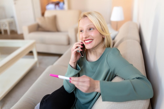 Finally pregnant Young women looking at pregnancy test and smiling while calling the father to give him happy news Young happy woman looking at a positive pregnancy test and calling husband by phone