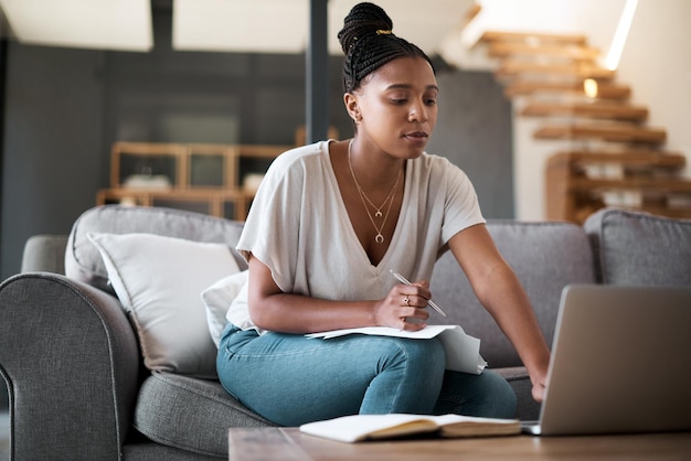 Finance laptop and black woman writing a house budget for bills savings or money management on living room sofa Paperwork inflation and African person planning financial taxes payment in notebook