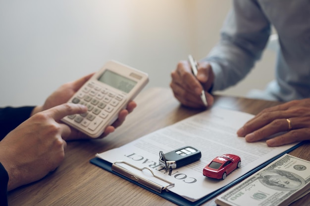 Photo finance manager of the car showroom is calculating the cost of reserving a new car for the customer while signing a car purchase contract