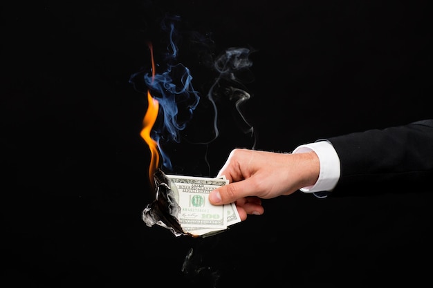 finances, people, savings and bankruptcy concept - close up of male hand holding burning dollar cash money over black background