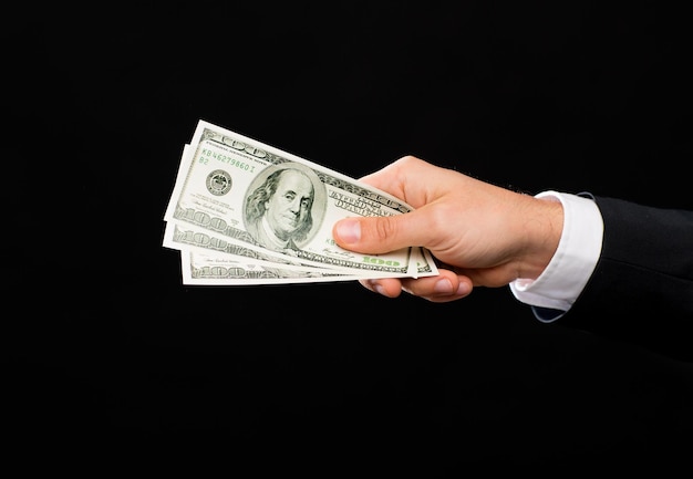 finances, people, savings and poverty concept - close up of male hand holding dollar cash money over black background