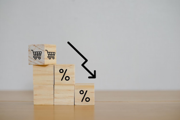 Financial crisis concept Wooden block signs and symbols and shopping cart on white background with percentage sign of store loss of income capital lost cost reduction declining chart down profit