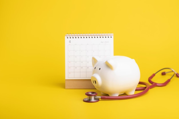 Financial for health concept The idea of saving money for healthcare Close up stethoscope 2023 calendar and white piggy bank on yellow Time for health check up and finance concept