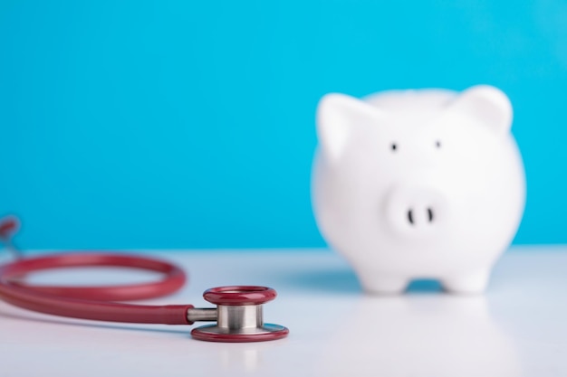 Financial for health concept The idea of saving money for healthcare Close up stethoscope and white piggy bank on wooden desk with color copy space Health and finance concept