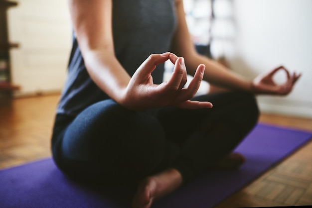 Finding my balance Cropped shot of an unrecognizable woman sitting on a yoga mat and meditating alone in her home