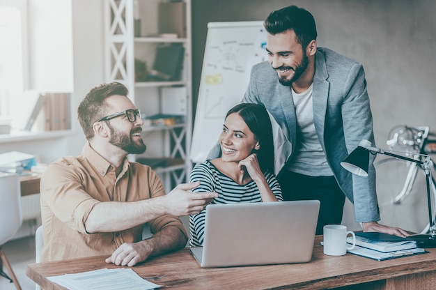 Finding solution together. Group of confident business people in smart casual wear discussing something while sitting at the desk in office