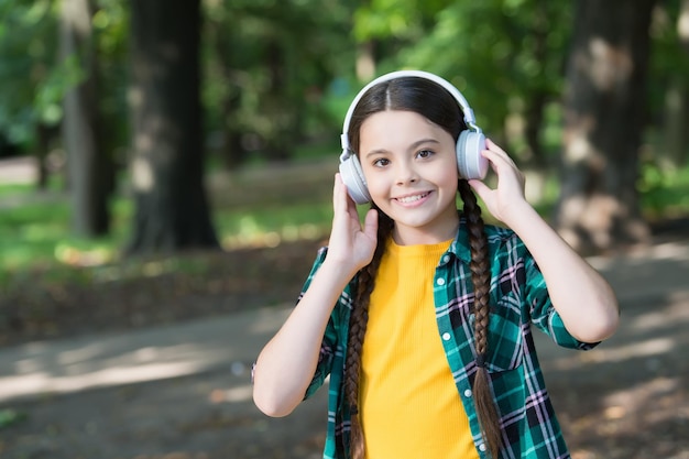 Fine engineering only for your ears Happy kid wear ear phones natural outdoors Little girl listen to music in headphones Ear and hearing care Modern life New technology Summer vacation