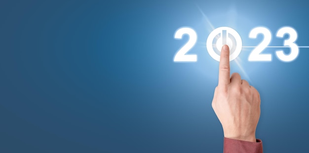 Finger pressing start 2023 button on virtual interface Businessman pressing 2023 start up business Beginning of New Year 2023 Hand presses start button of new year copy space blue background