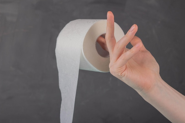 On the finger of a woman's hand holding a roll of toilet paper on a gray background