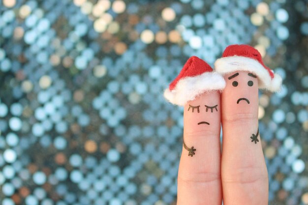 Photo fingers art of displeased couple celebrates christmas. concept of sad man and woman in new year hats.