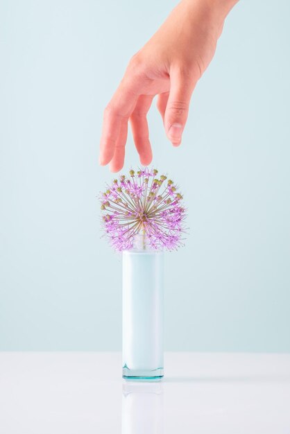 Fingers of a female hand reach for a cosmetic white cream in a bottle on a white-blue background, minimal concept.