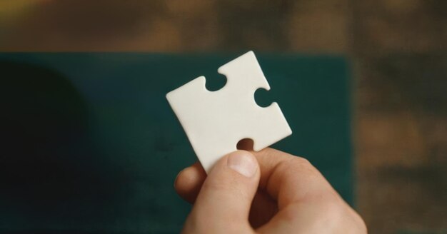 Fingers holding a piece of a white puzzle