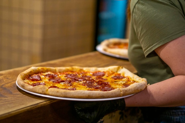 The finished pizza is picked up by a waitress in a mask and gloves from the kitchen to bring to customers