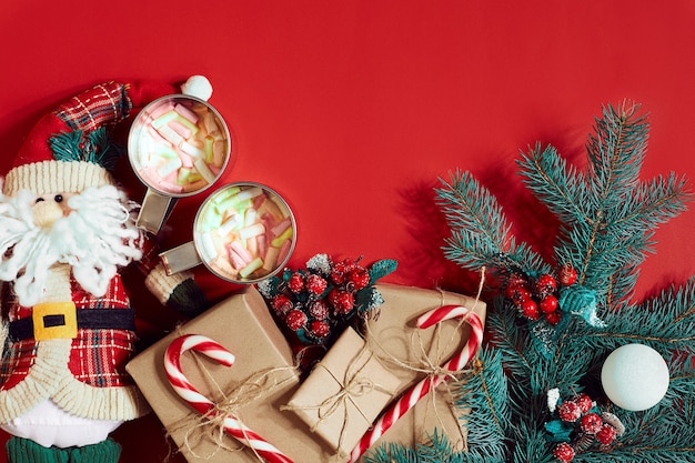 Fir branch, gift box and two cups of cocoa with marshmallows on red background. Top view. Flat lay. Copy space. Still life. Christmas and New year