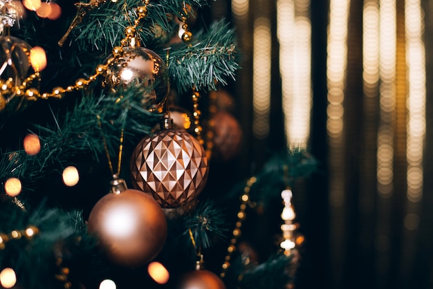 Fir branch with golden balls and festive lights on the dark background with sparkles.