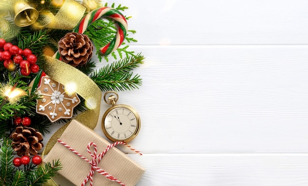 Fir tree branches, Retro style clock, christmas decorations and gift on white wooden background. Last moments before Christmas or New Year. New Year's Eve. Top view. Copy space