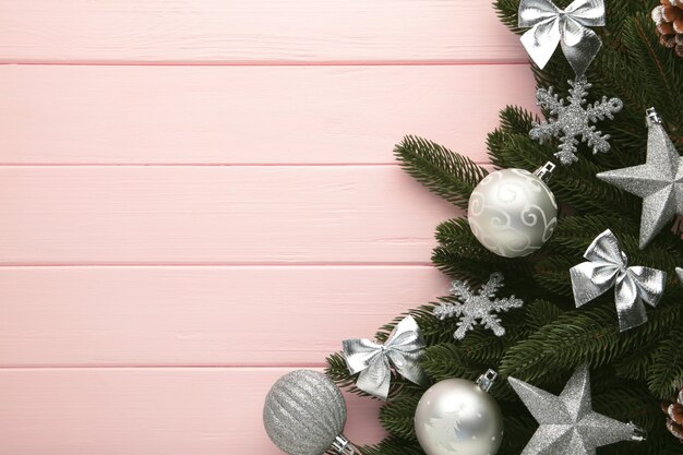 Fir-tree branches with silver christmas decorations on pink background with copy space