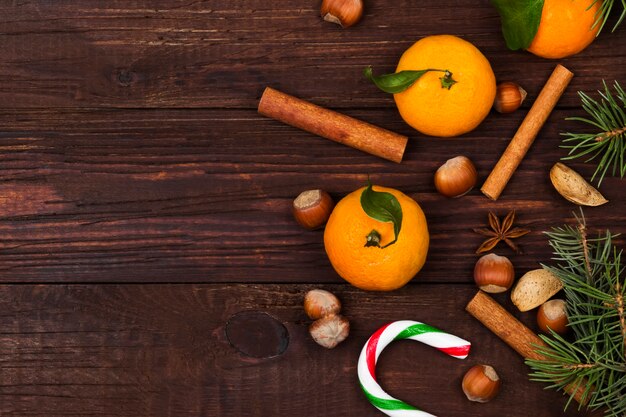 fir-tree, tangerines, candy cane, cinnamon, almonds on dark wood, Top view, copy space