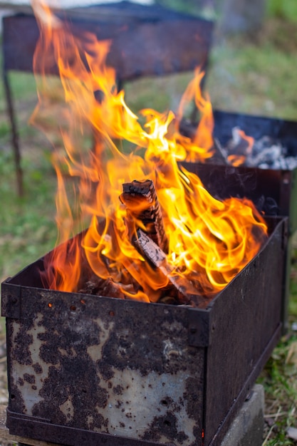 A fire is burning in a metal grill. A large, bright flame of fire at close range. Outdoor recreation. 5