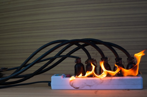 On fire multi socket with the connected power strip with a bunch of plugs on wood background