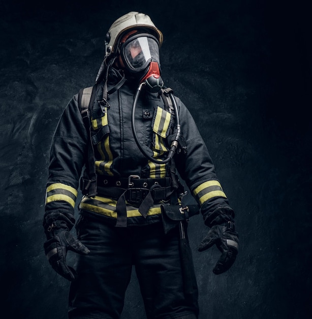 Firefighter in safety helmet and oxygen mask wearing protective clothes. Studio photo against a dark textured wall