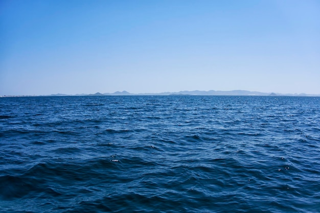 Firm land and mountains seen in the distance from a calm sea on a sunny day with a clear sky and blue sky