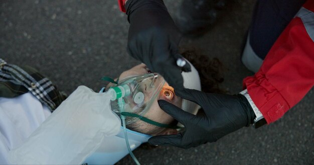 Photo first aid paramedic and check man with flashlight for emergency ems service accident and oxygen mask hands medical or light on unconscious patient eyes for healthcare help or rescue in top view