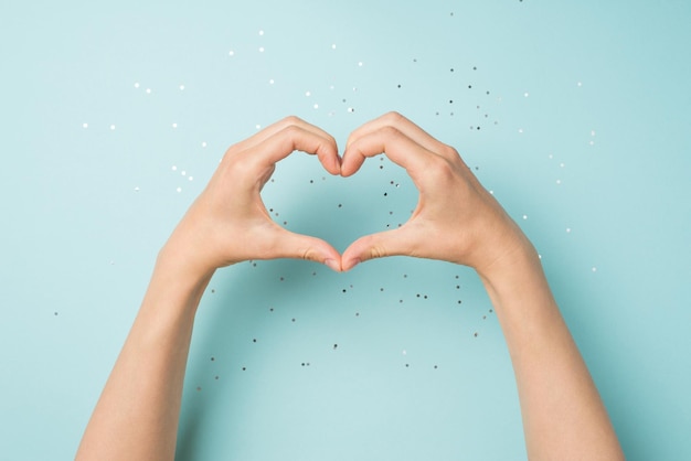 First person top view photo of female hands making heart with fingers on isolated pastel blue background with copyspace