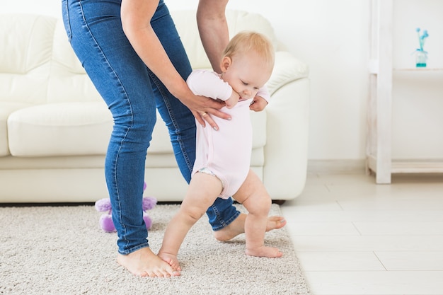 First steps of baby toddler learning to walk in white sunny living room. Footwear for child.