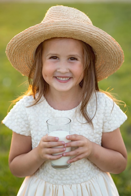 Firstgrader schoolgirl in hat drinks milk from glass smiling