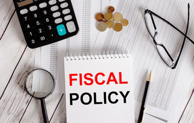 FISCAL POLICY written in a white notepad near a calculator, cash, glasses, a magnifying glass and a pen