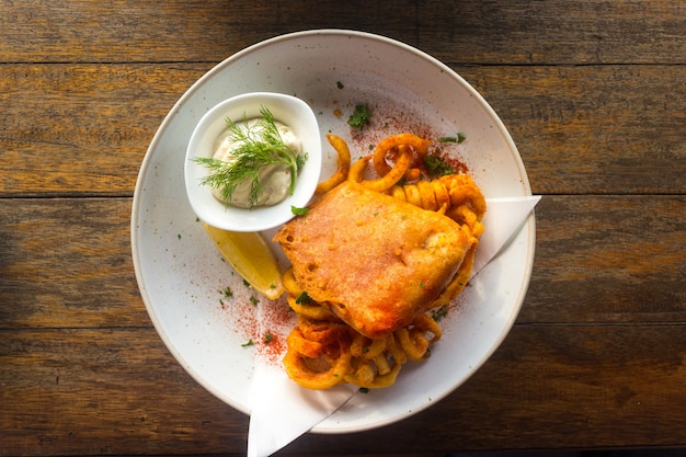 Fish and chips with tartar sauce in a plate on a wooden table