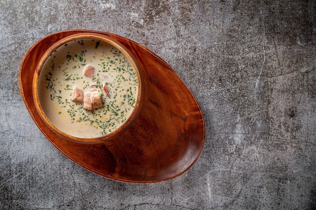 Fish cream soup of salmon with herbs in a wooden bowl on a tray against a gray stone table