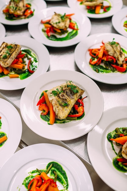 Fish dish with vegetables for catering. Lots of plates.