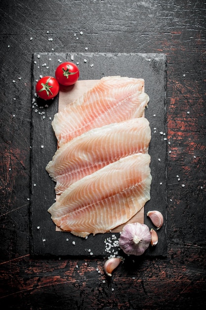 Photo fish fillet on paper on a stone board with garlic and tomatoes