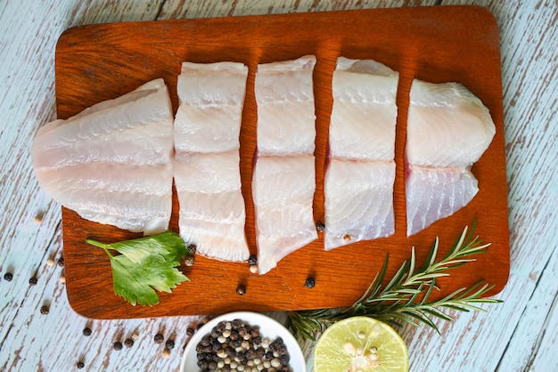 Fish fillet on wooden board with ingredients for cooking fresh raw pangasius fish fillet with herb and spices black pepper lemon lime and rosemary meat dolly fish tilapia striped catfish