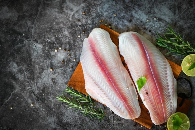 Fish fillet on wooden board with ingredients for cooking meat dolly fish tilapia striped catfish fresh raw pangasius fish fillet with herb and spices black pepper lemon lime