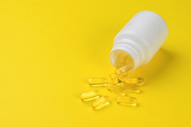 Fish oil capsules spilling out of a white jar on a yellow background