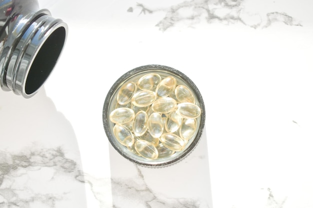 Fish oil capsules with omega3 and vitamin D in a jar on a white concrete surface