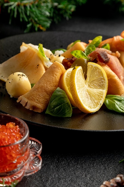 Fish platter on a black plate with red caviar on a dark Christmas background with Christmas toys and spruce branches