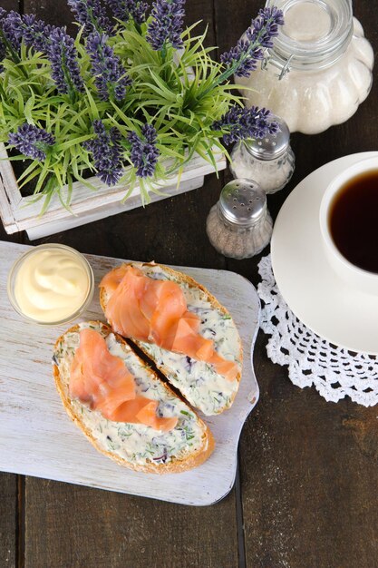 Fish sandwiches and cup of tea on cutting board on wooden table