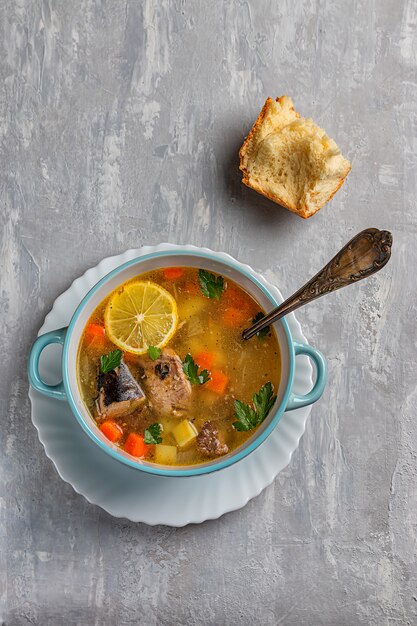 Fish soup with potatoes and carrots, on a concrete background with a slice of lemon and bread