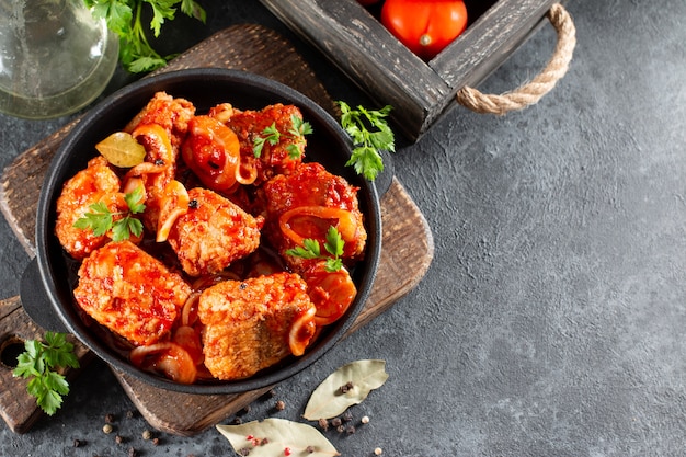 Fish in tomato sauce with lemon and parsley in a frying pan. Horizontal view from above, with copy space